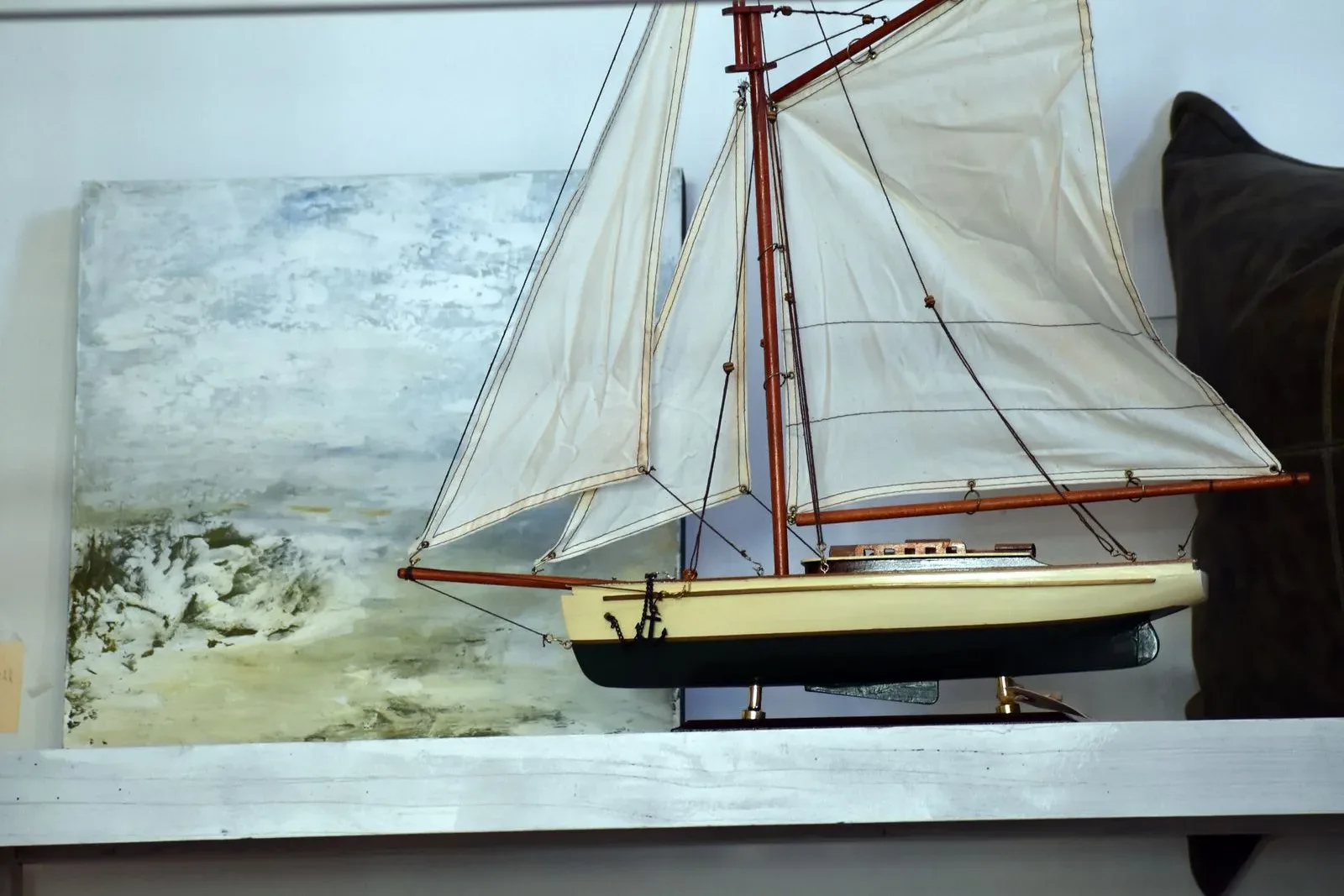 Miniature sailboat model with cream sails displayed on a shelf